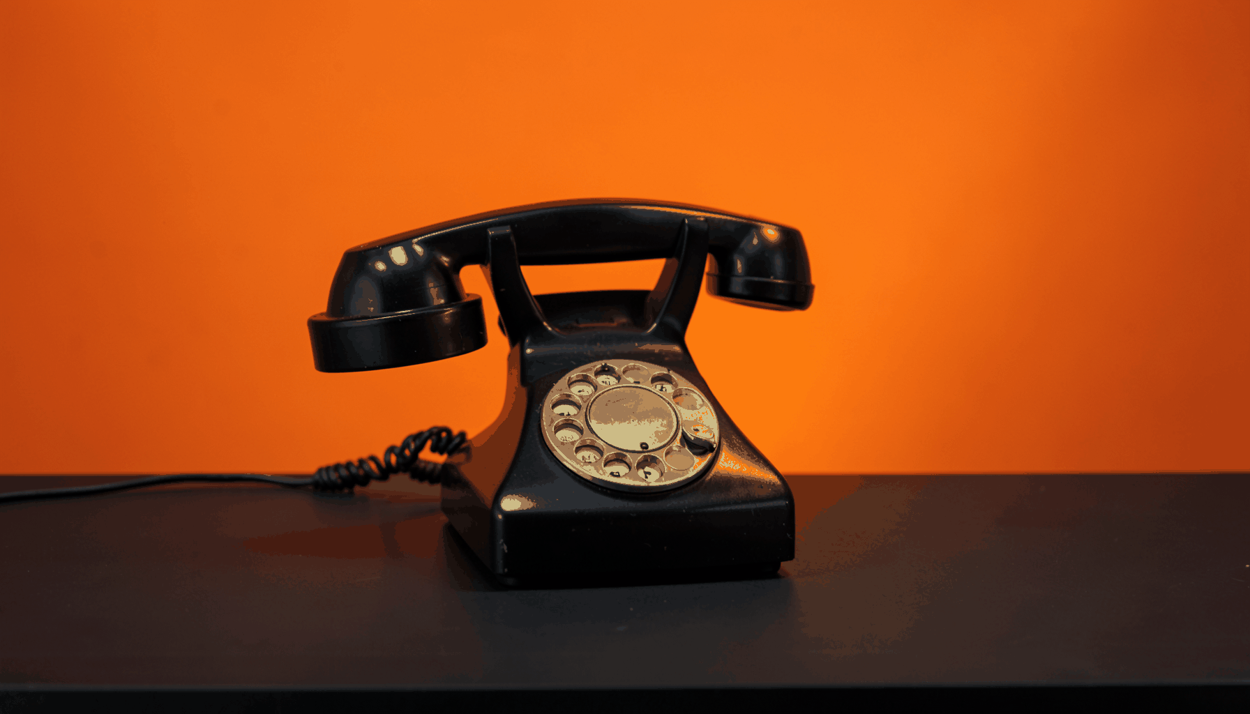 A single vintage rotary telephone on a dark charcoal desk, warm gold accent light, formal and understated